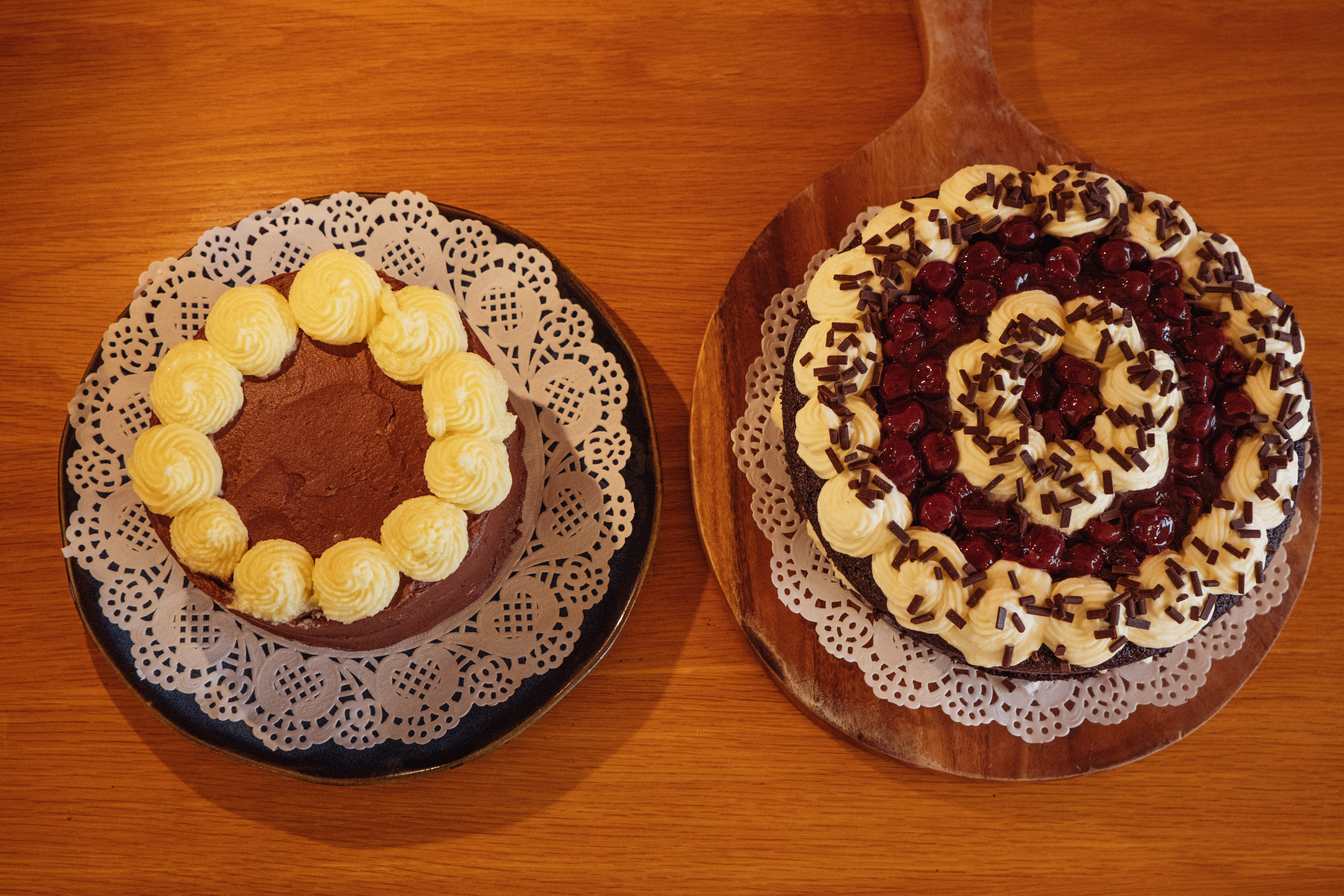 Overhead size comparison: a 20 cm vanilla cake with chocolate frosting on the left and a 25 cm Black Forest cake on the right